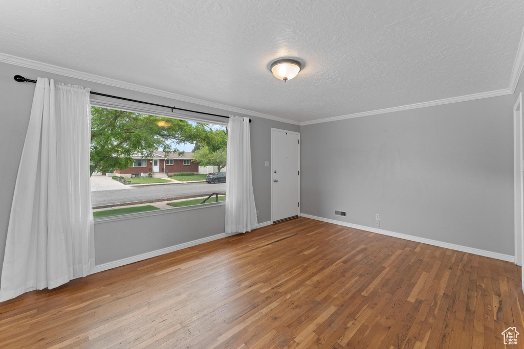 Spare room featuring wood finished floors, a textured ceiling, baseboards, and ornamental molding