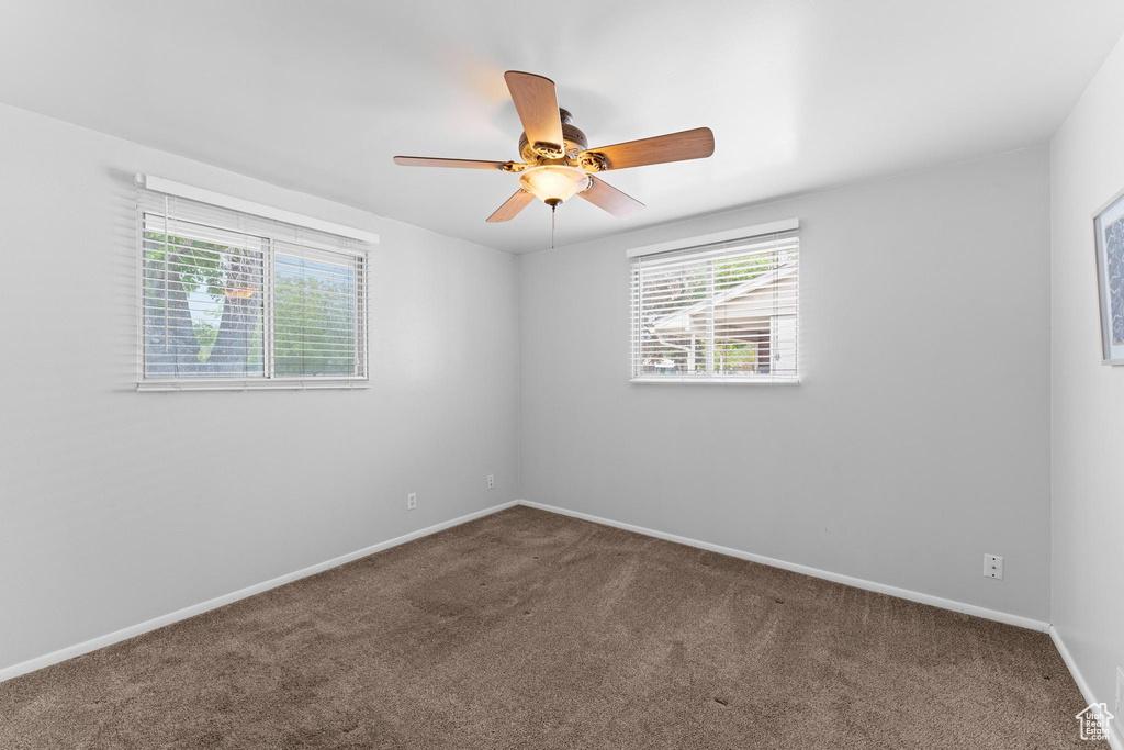 Carpeted empty room with healthy amount of natural light, a ceiling fan, and baseboards