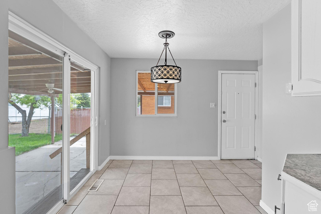 Unfurnished dining area with baseboards, a textured ceiling, and light tile patterned flooring