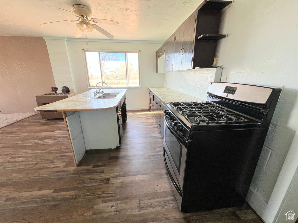 Kitchen featuring gas range, a sink, dark wood-style floors, light countertops, and an island with sink
