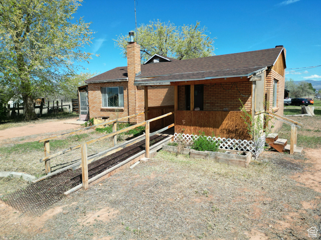 Back of house featuring a chimney, roof with shingles, and brick siding