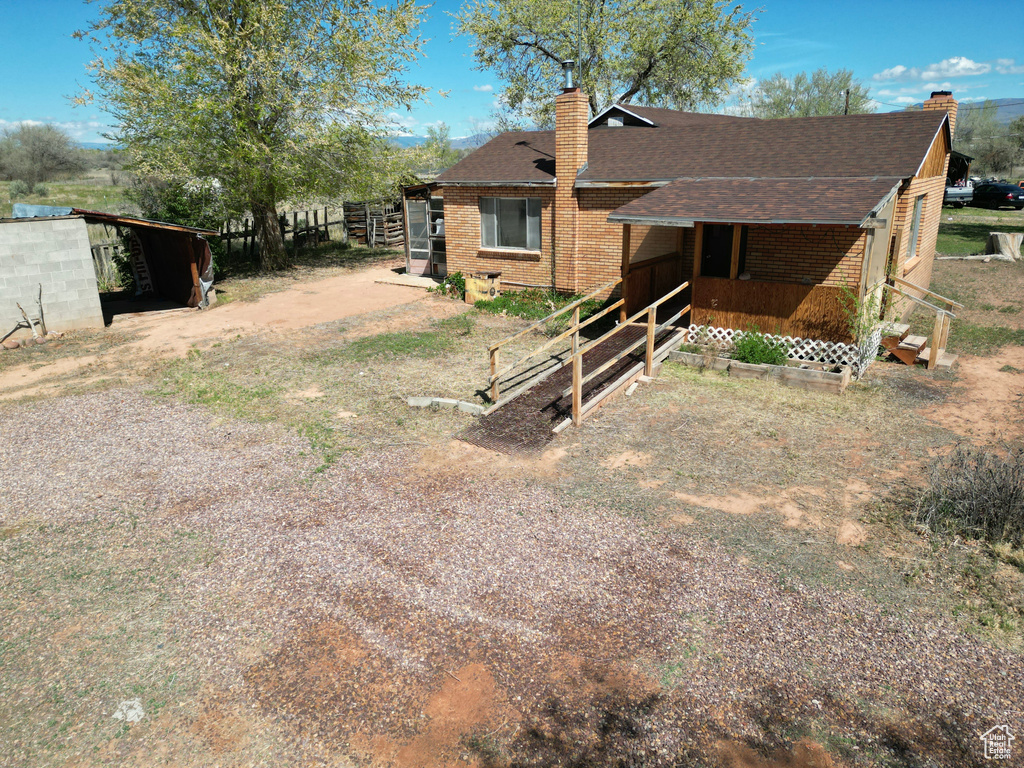 Rear view of property with a chimney, roof with shingles, brick siding, and driveway
