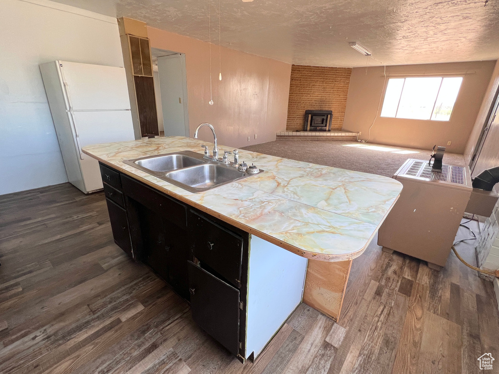 Kitchen with freestanding refrigerator, a sink, dark wood-type flooring, a textured ceiling, and dark cabinetry