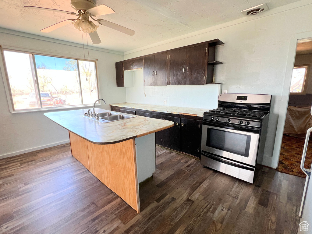 Kitchen with stainless steel gas stove, a sink, light countertops, and dark wood-type flooring