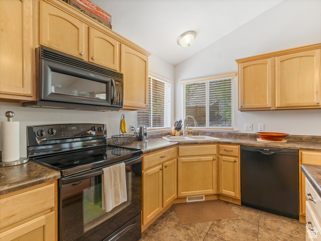 Kitchen with black appliances, a sink, lofted ceiling, light brown cabinetry, and dark countertops