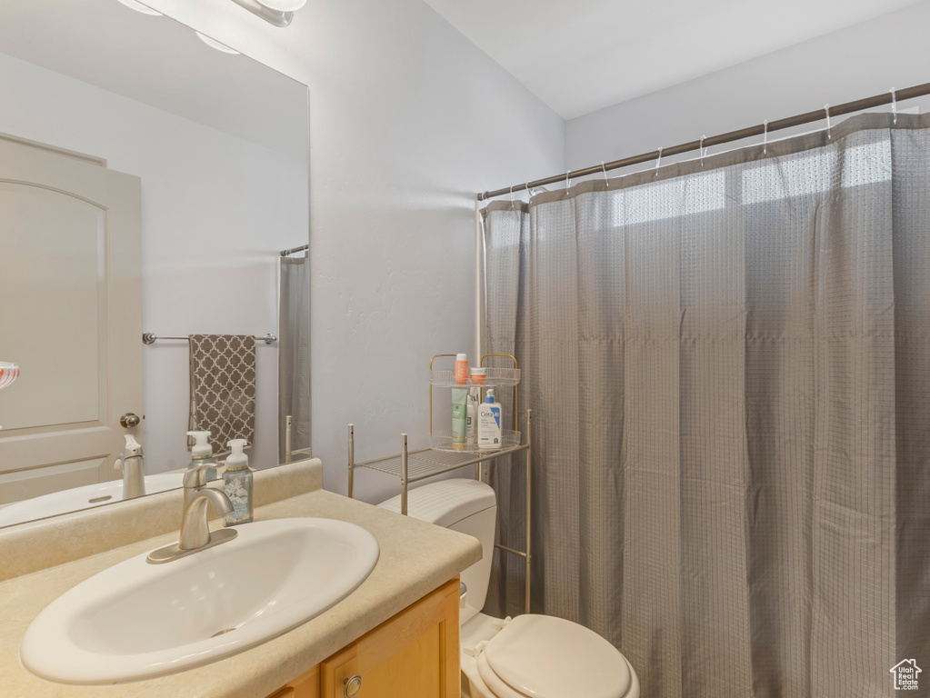Bathroom with toilet, vanity, and curtained shower