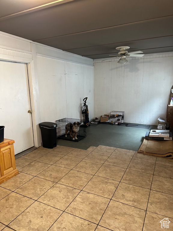 Below grade area featuring ceiling fan, light tile patterned floors, and wooden walls