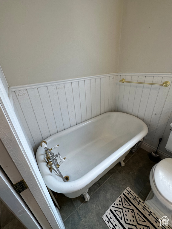 Full bath with toilet, a freestanding bath, tile patterned flooring, and a wainscoted wall