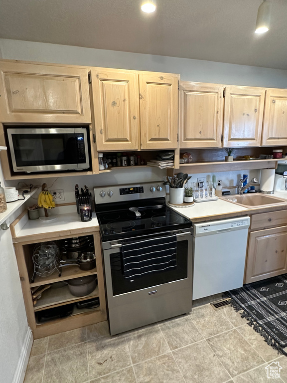 Kitchen with stainless steel appliances, a sink, light brown cabinetry, and light countertops