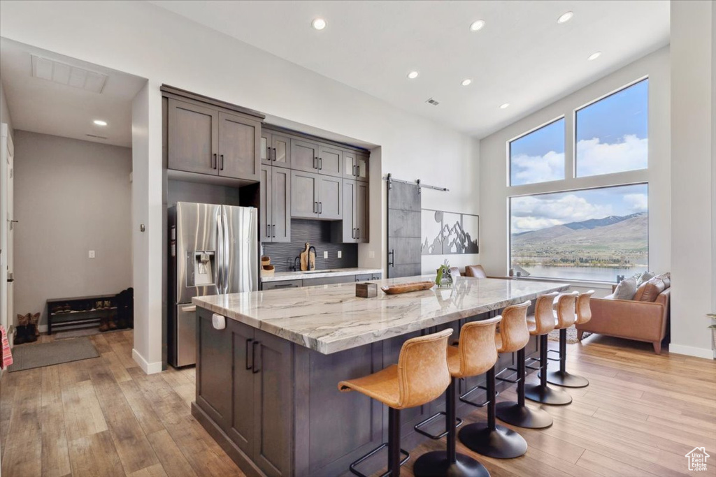 Kitchen featuring stainless steel refrigerator with ice dispenser, a center island, light stone counters, light wood-type flooring, and recessed lighting
