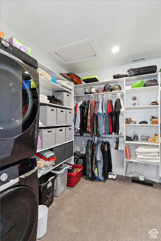 Walk in closet with stacked washer / drying machine, attic access, and carpet flooring