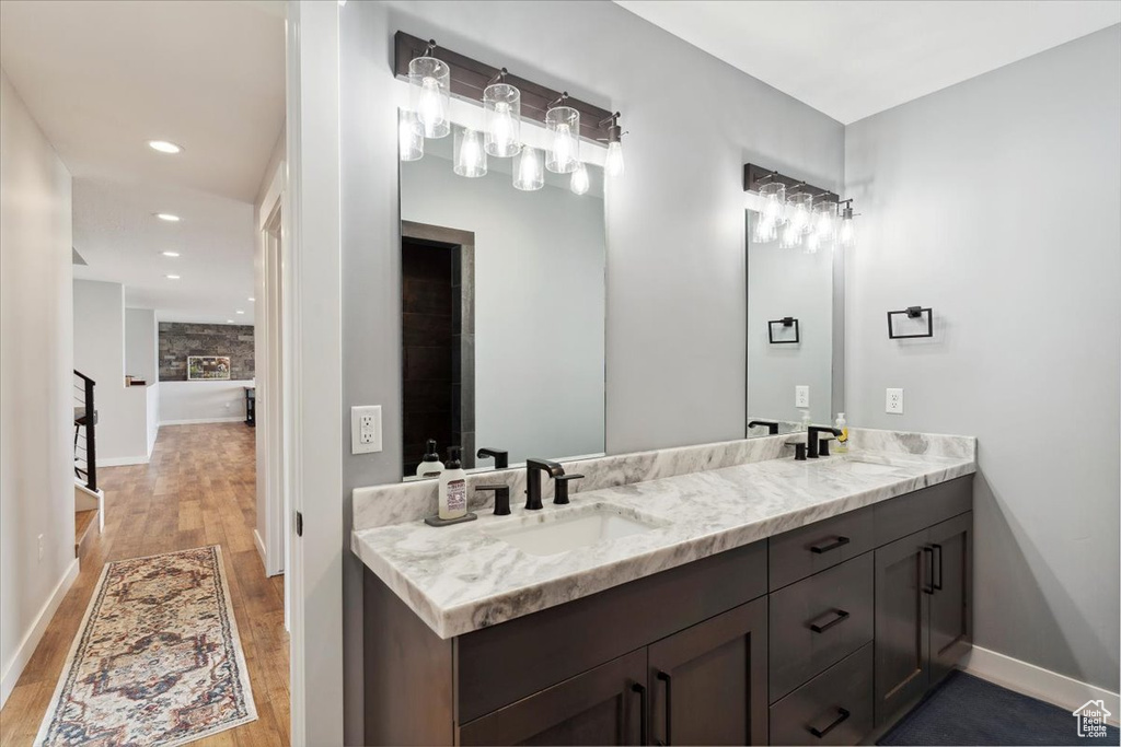Bathroom featuring wood finished floors, double vanity, baseboards, and recessed lighting