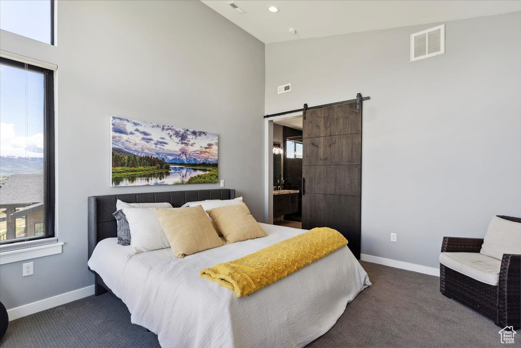Carpeted bedroom featuring high vaulted ceiling, a barn door, baseboards, multiple windows, and ensuite bathroom