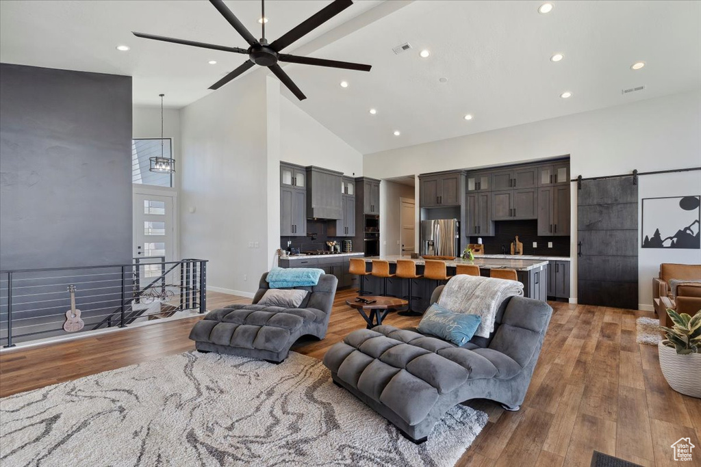 Living area featuring high vaulted ceiling, a ceiling fan, recessed lighting, wood finished floors, and a barn door