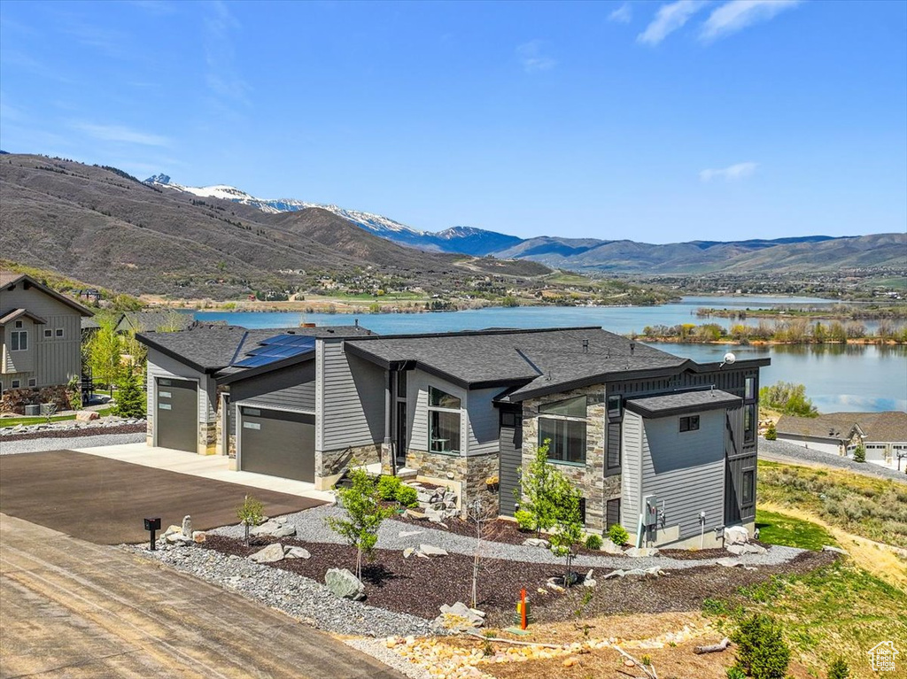 View of front of house featuring a garage, a water and mountain view, stone siding, driveway, and roof with shingles