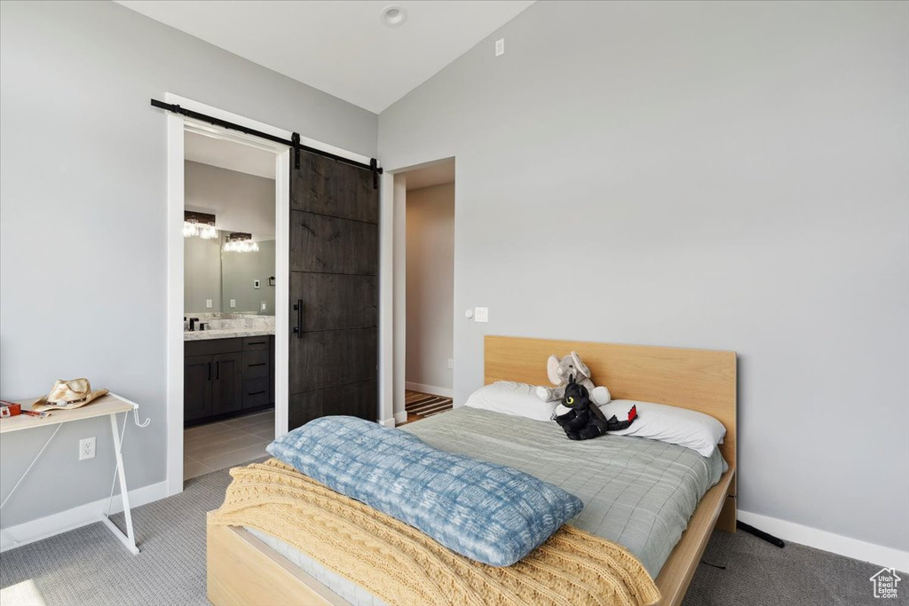 Bedroom with a barn door, vaulted ceiling, baseboards, and light carpet
