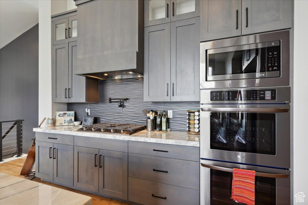 Kitchen featuring stainless steel appliances, backsplash, light stone countertops, and glass insert cabinets