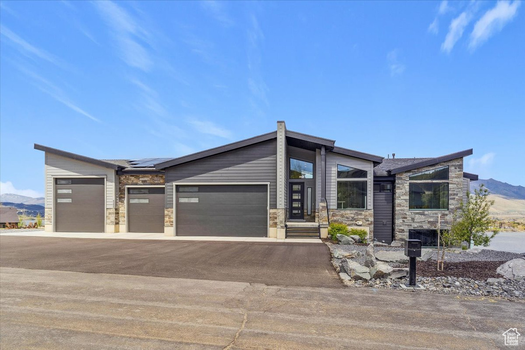 Contemporary house featuring stone siding, asphalt driveway, roof mounted solar panels, an attached garage, and a mountain view