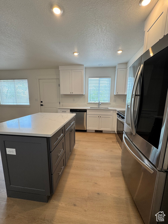 Kitchen with appliances with stainless steel finishes, a sink, white cabinetry, a textured ceiling, and a kitchen island