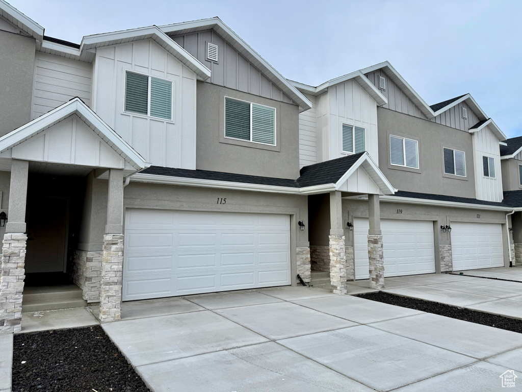 Townhome / multi-family property with board and batten siding, an attached garage, and stone siding
