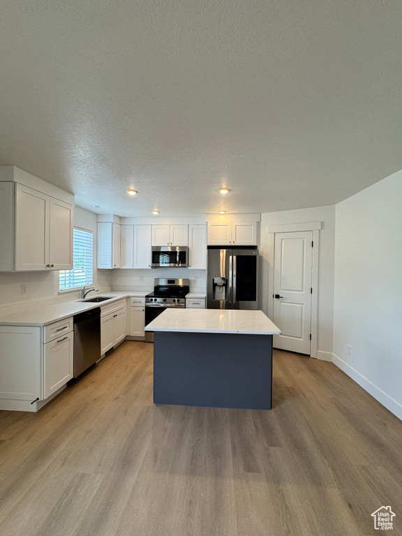 Kitchen with appliances with stainless steel finishes, a kitchen island, light wood-style floors, baseboards, and a textured ceiling