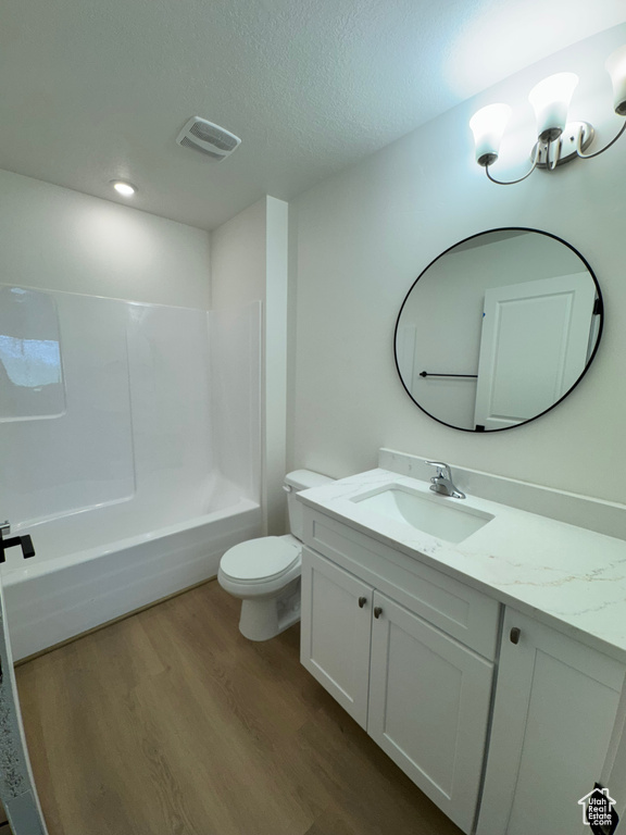 Bathroom featuring wood finished floors, vanity, toilet, a textured ceiling, and bathtub / shower combination