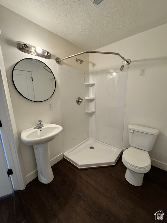 Bathroom with wood finished floors, a textured ceiling, a stall shower, baseboards, and toilet