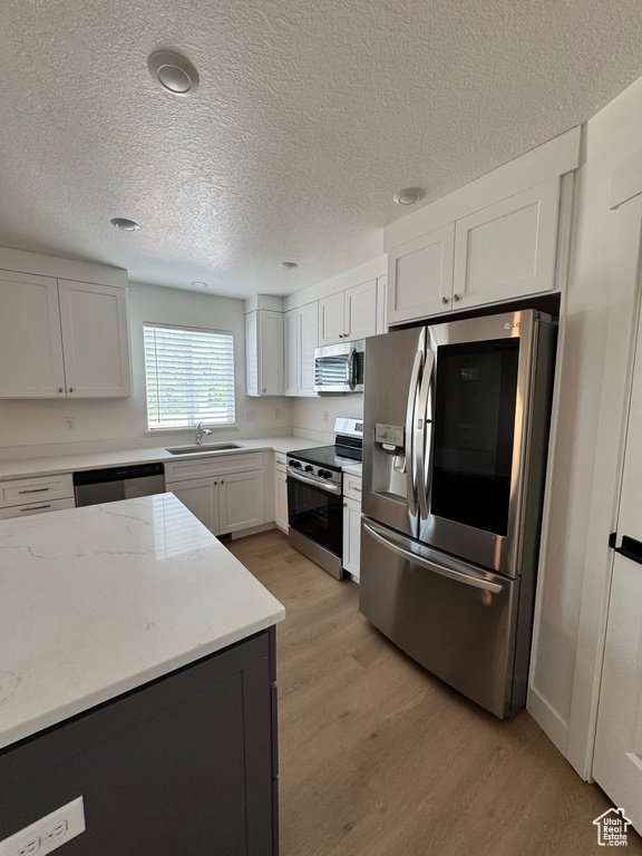 Kitchen featuring appliances with stainless steel finishes, a sink, light wood-style floors, white cabinets, and a textured ceiling