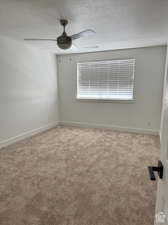 Carpeted empty room featuring ceiling fan, a textured ceiling, and baseboards