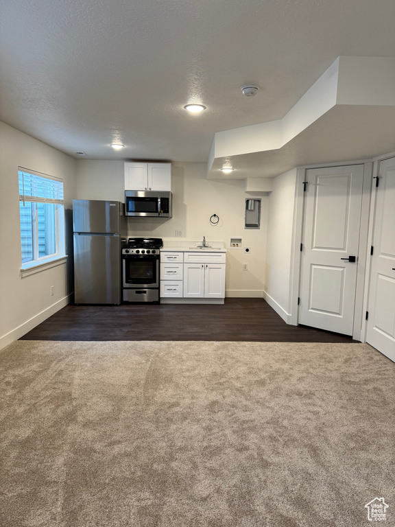 Kitchen featuring appliances with stainless steel finishes, dark carpet, a sink, baseboards, and a textured ceiling