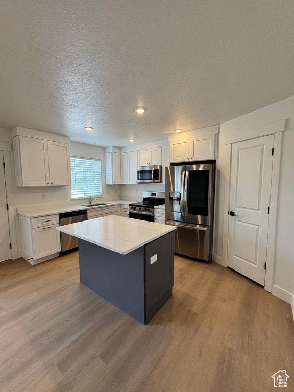 Kitchen featuring appliances with stainless steel finishes, a sink, light wood-style floors, a textured ceiling, and white cabinets