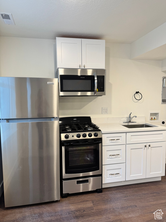 Kitchen featuring appliances with stainless steel finishes, a sink, white cabinetry, and light countertops