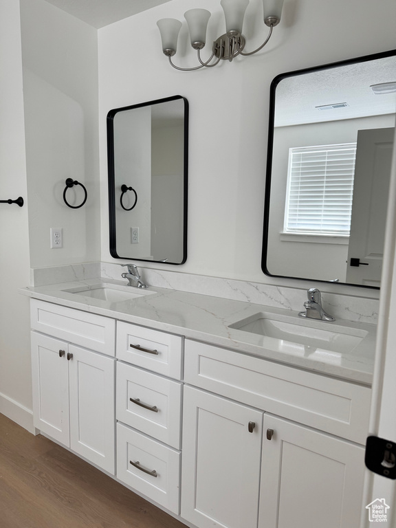 Bathroom with wood finished floors, double vanity, and a chandelier