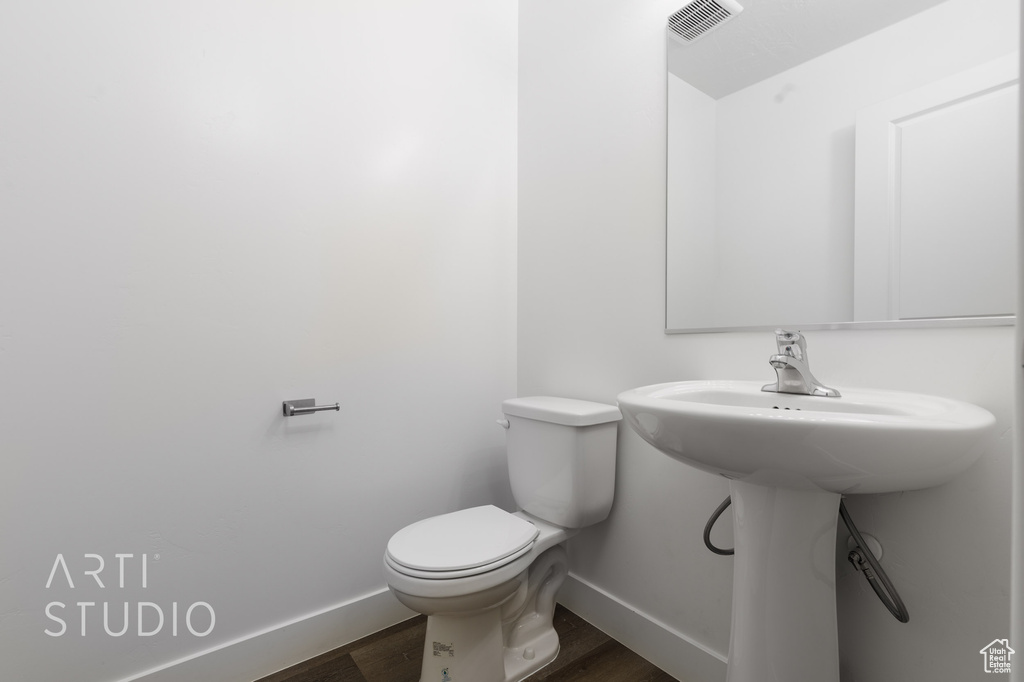 Half bath with baseboards, wood finished floors, and toilet