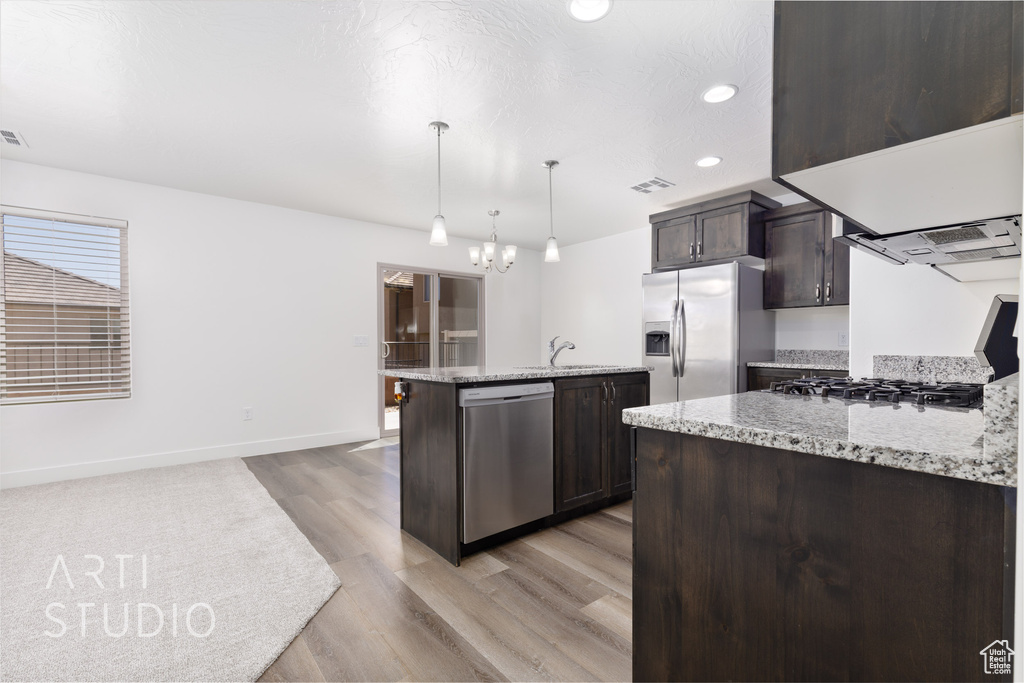 Kitchen with appliances with stainless steel finishes, dark brown cabinetry, baseboards, light wood finished floors, and light stone counters