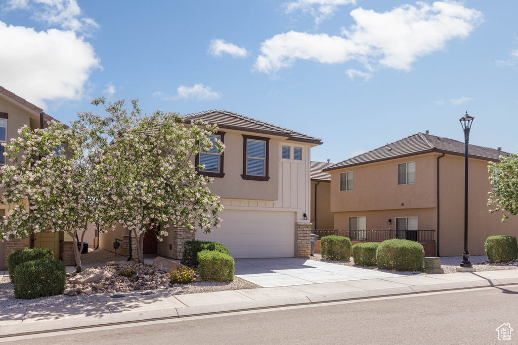 View of front facade with a garage, concrete driveway, stucco siding, fence, and stone siding