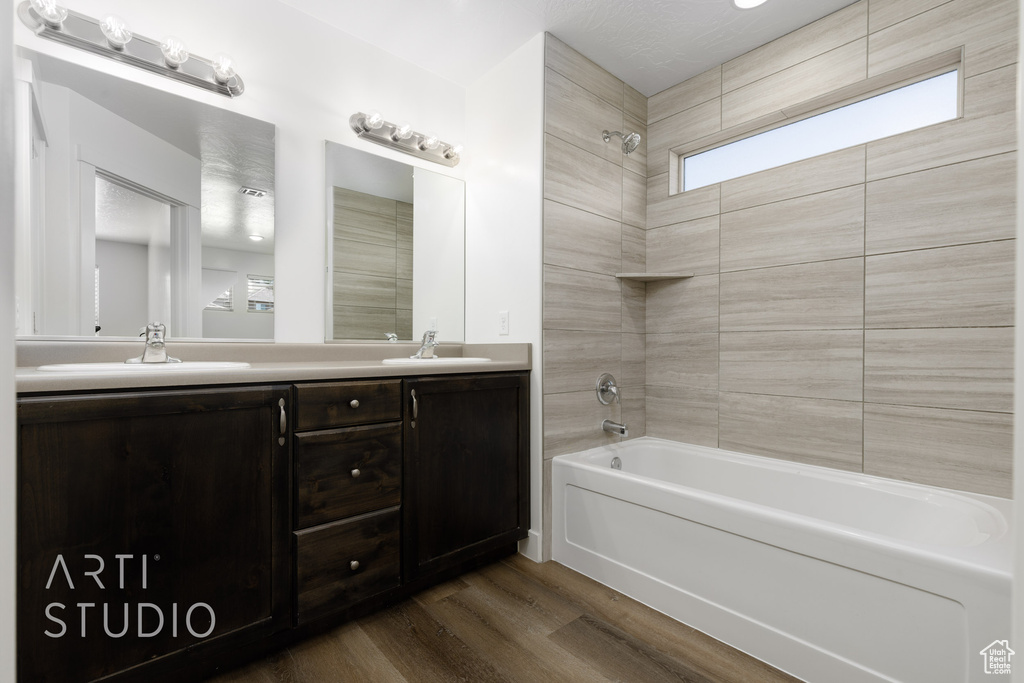 Bathroom with shower / bathtub combination, wood finished floors, and double vanity