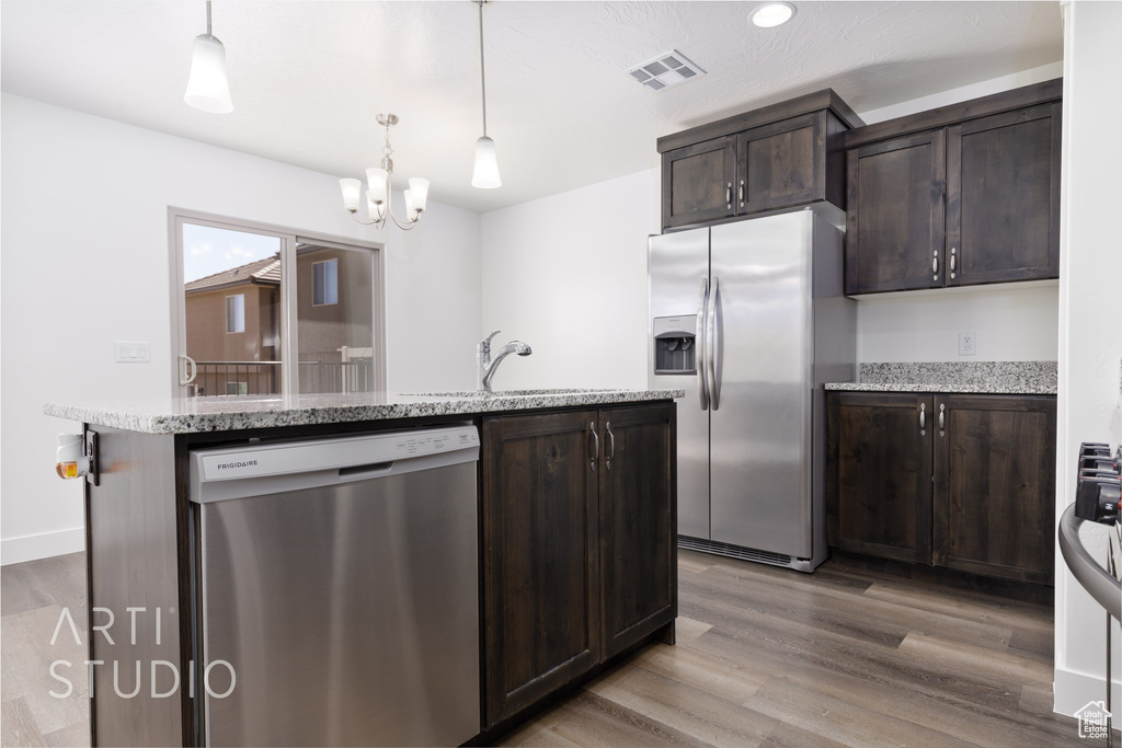 Kitchen with appliances with stainless steel finishes, dark brown cabinetry, a center island with sink, a chandelier, and pendant lighting