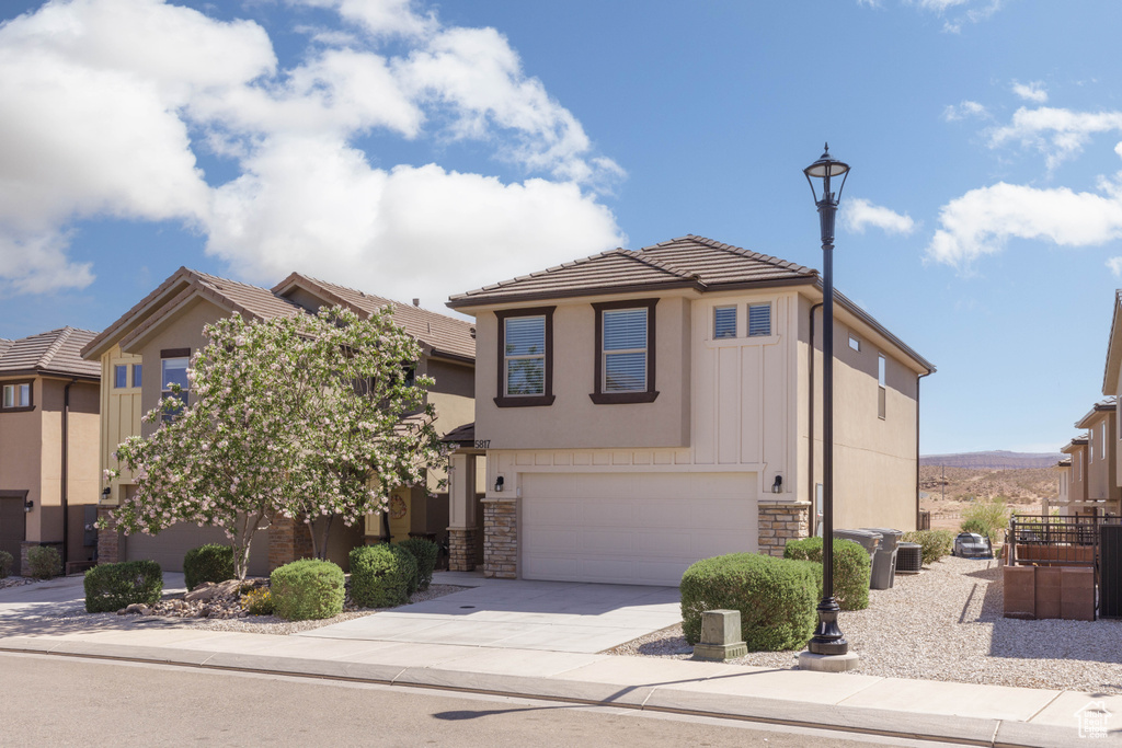 View of front of home with an attached garage, stone siding, concrete driveway, a tiled roof, and stucco siding