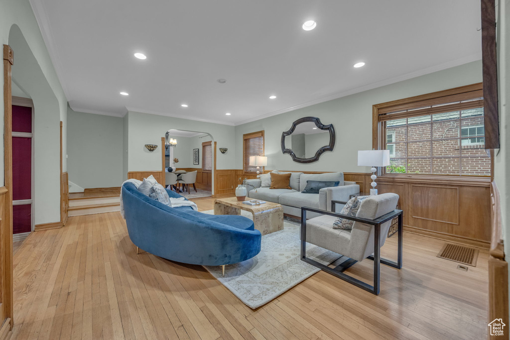 Living area with arched walkways, wainscoting, plenty of natural light, crown molding, and light wood-style flooring