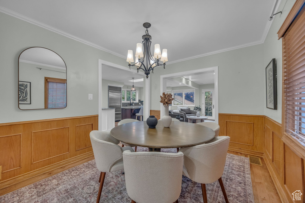 Dining room with wainscoting, a chandelier, light wood-style flooring, and crown molding