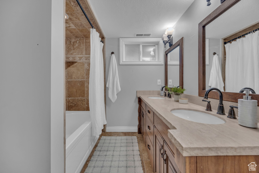 Full bathroom with baseboards, double vanity, shower / bath combo with shower curtain, and tile patterned flooring