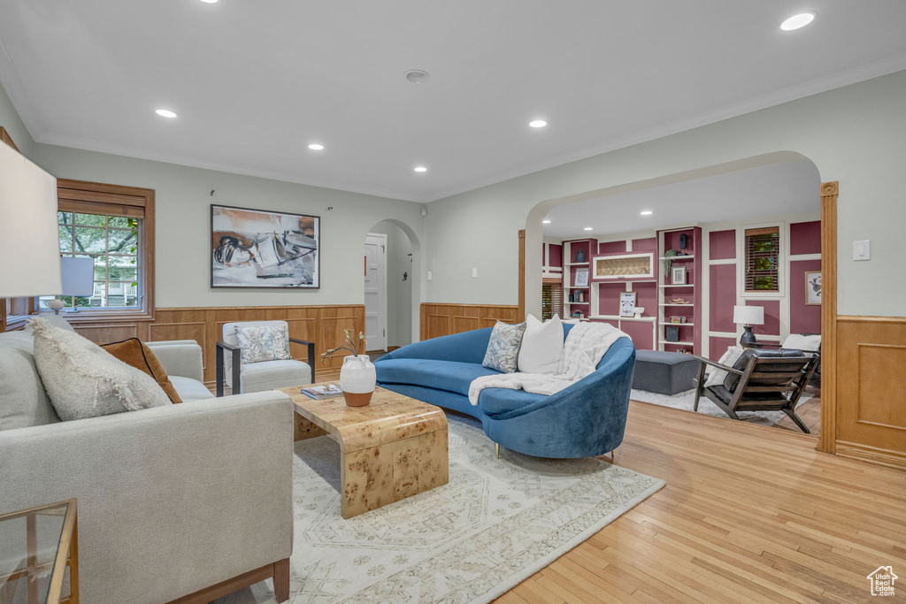 Living area with arched walkways, a wainscoted wall, recessed lighting, light wood-style floors, and ornamental molding