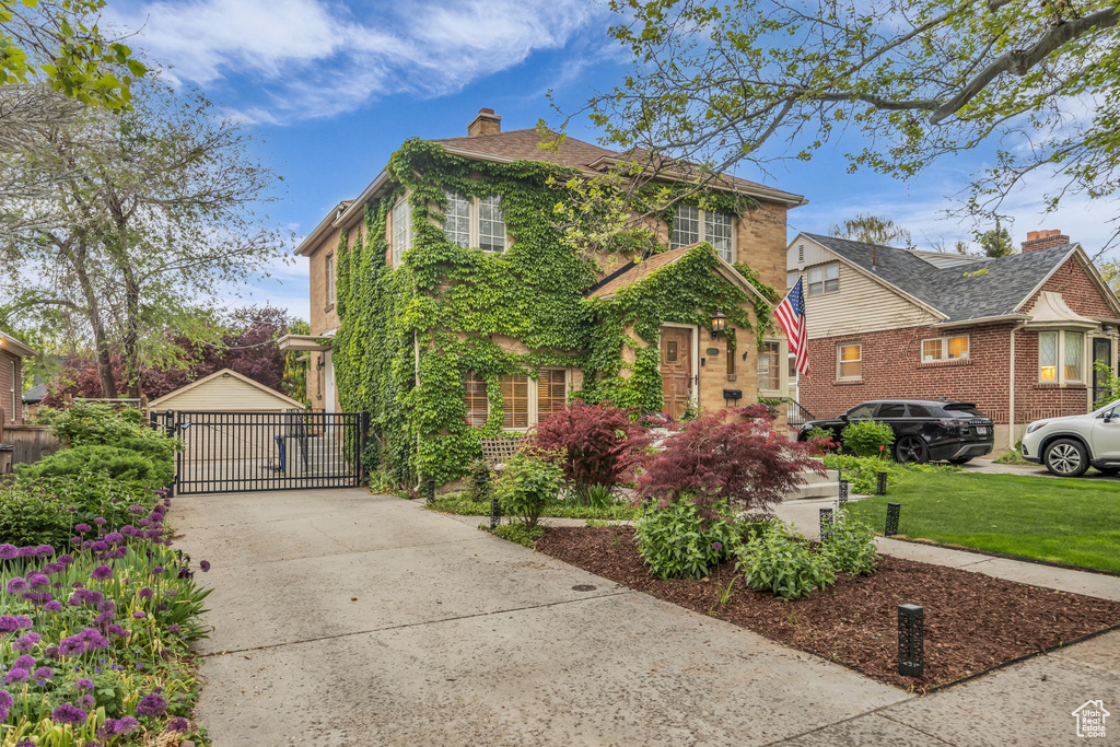 View of front of property featuring a chimney, a front yard, brick siding, and an outbuilding