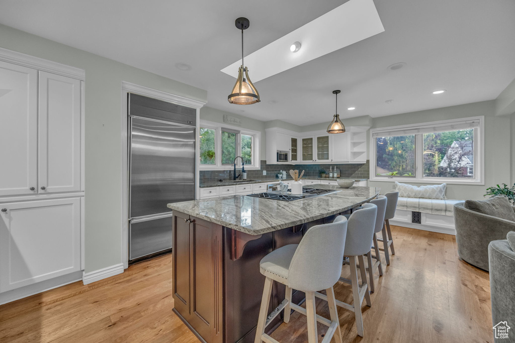 Kitchen featuring stainless steel appliances, a sink, white cabinetry, light stone countertops, and decorative backsplash