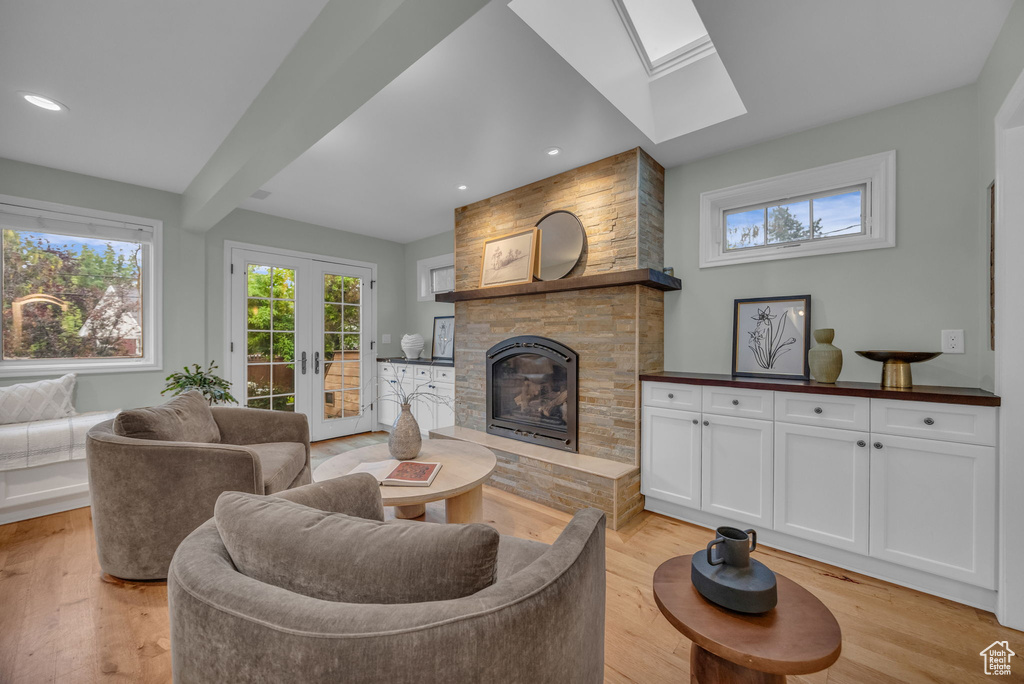 Living room featuring a skylight, a glass covered fireplace, light wood-style floors, beam ceiling, and french doors