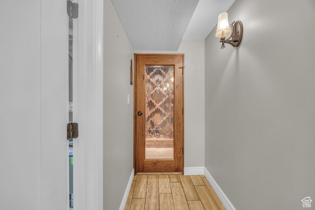 Doorway with light wood-type flooring, baseboards, and a textured ceiling