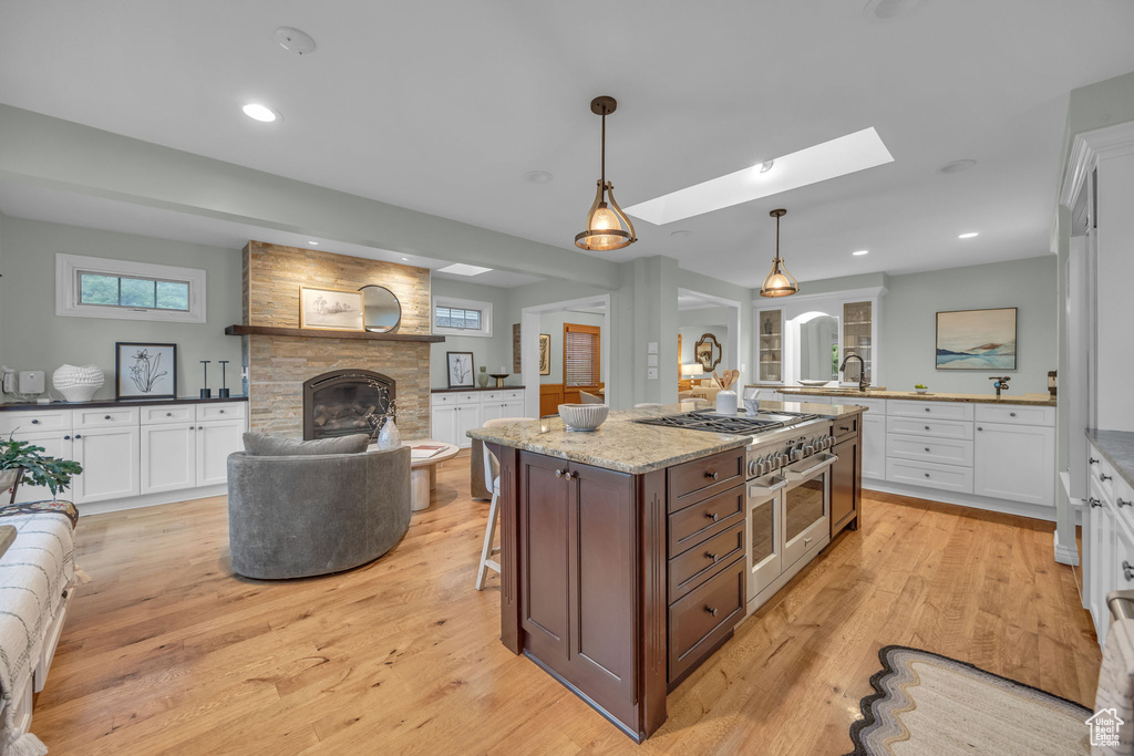 Kitchen featuring a stone fireplace, white cabinets, a skylight, light wood-style floors, and recessed lighting