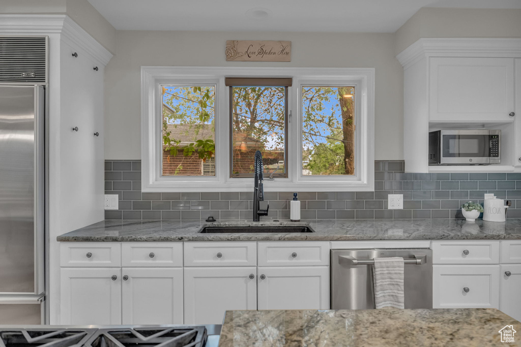 Kitchen with a sink, stainless steel appliances, tasteful backsplash, white cabinetry, and light stone countertops