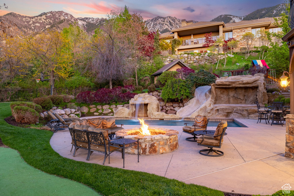 Patio terrace at dusk with a fire pit, a mountain view, and an outdoor pool
